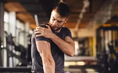 Young man feeling the pain in shoulder at the gym. How Much Does Private Shoulder Replacement Surgery Cost?