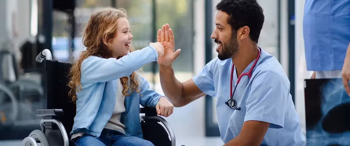 Young multiracial doctor having fun with little girl on wheelchair. Costs to see private consultants in the UK.