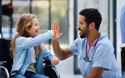 Young multiracial doctor having fun with little girl on wheelchair. Costs to see private consultants in the UK.