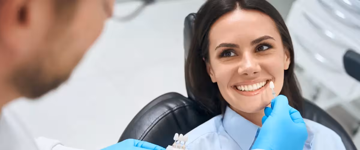 Woman sitting in dentist chair having a veneer fitted. Veneers Vs. Crowns - Pros And Cons And Costs