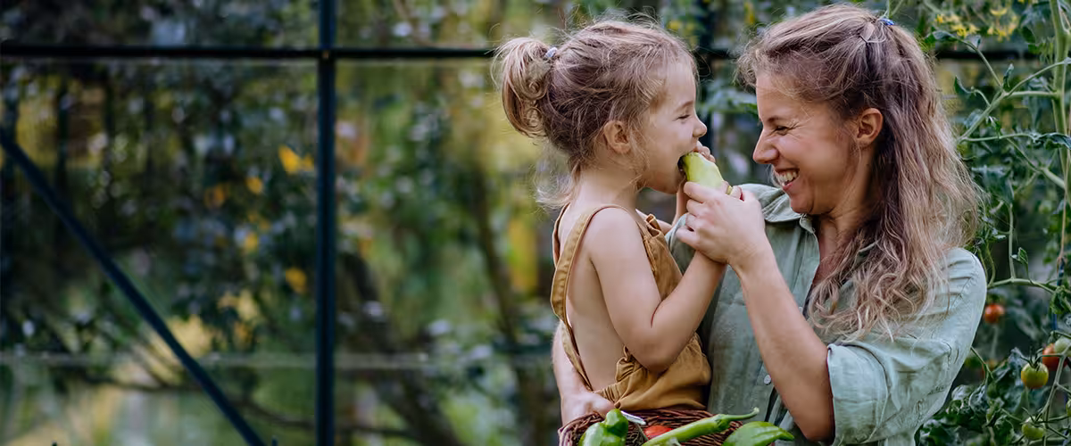 Happy mother with little daughter tasting fresh harvest when standing in a greenhouse. AXA Health Plan 2025 Review - An Expert Guide
