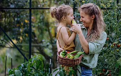 Happy mother with little daughter tasting fresh harvest when standing in a greenhouse. AXA Health Plan 2025 Review - An Expert Guide
