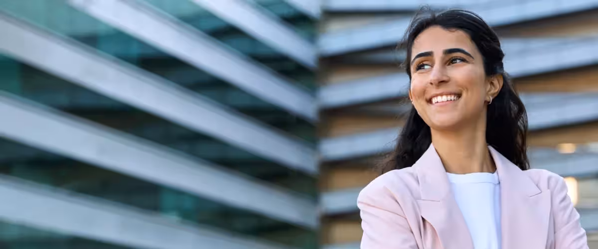 Young woman, wearing work wear, standing outside tall buildings, smiling. What is Relevant Life Cover? Life Insurance For Small Business Owners.