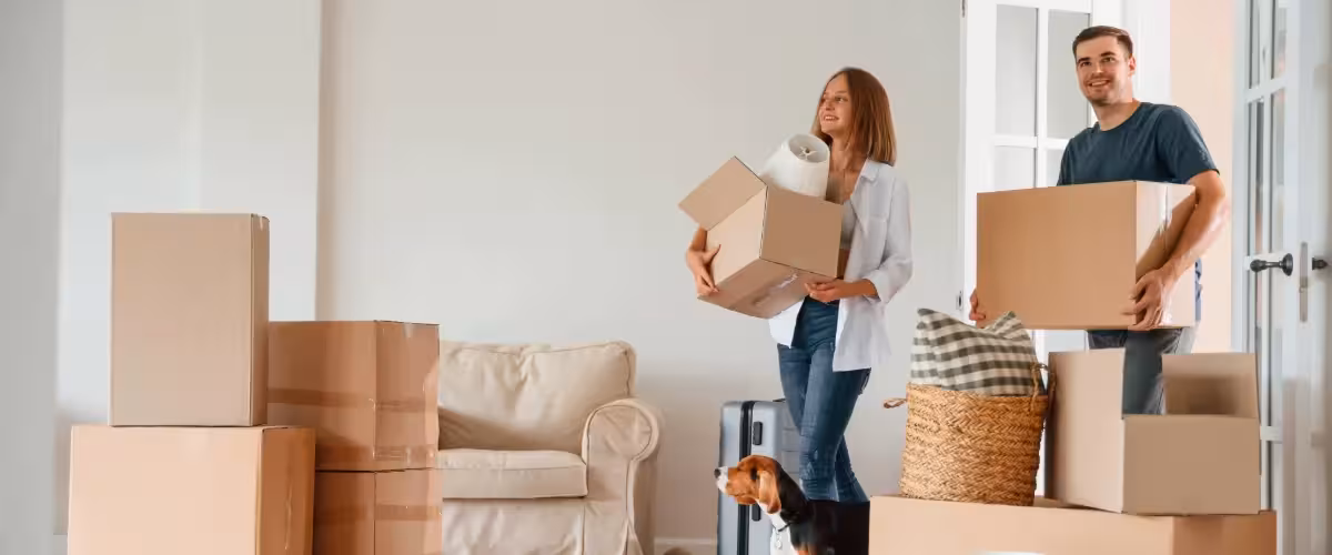 Smiling young couple with small dog moving into a new home carrying boxes, sofa and boxes in the background. Do You Have To Get Life Insurance When You Get A Mortgage?