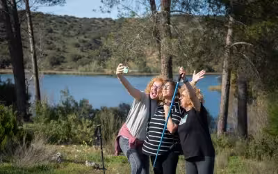 Three smiling sisters taking a selfie by a lagoon with trees holding walking poles. Top 6 Over 50s Life Insurance Plans In 2025 UK (myTribe Expert Review)