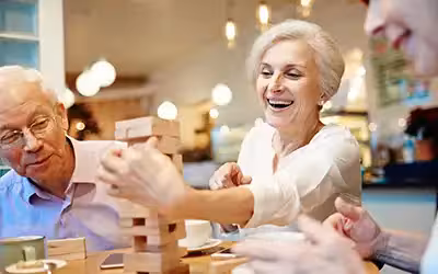 Happy mature friends enjoying playing Jenga together. How Does Life Insurance Work For Seniors In The UK?