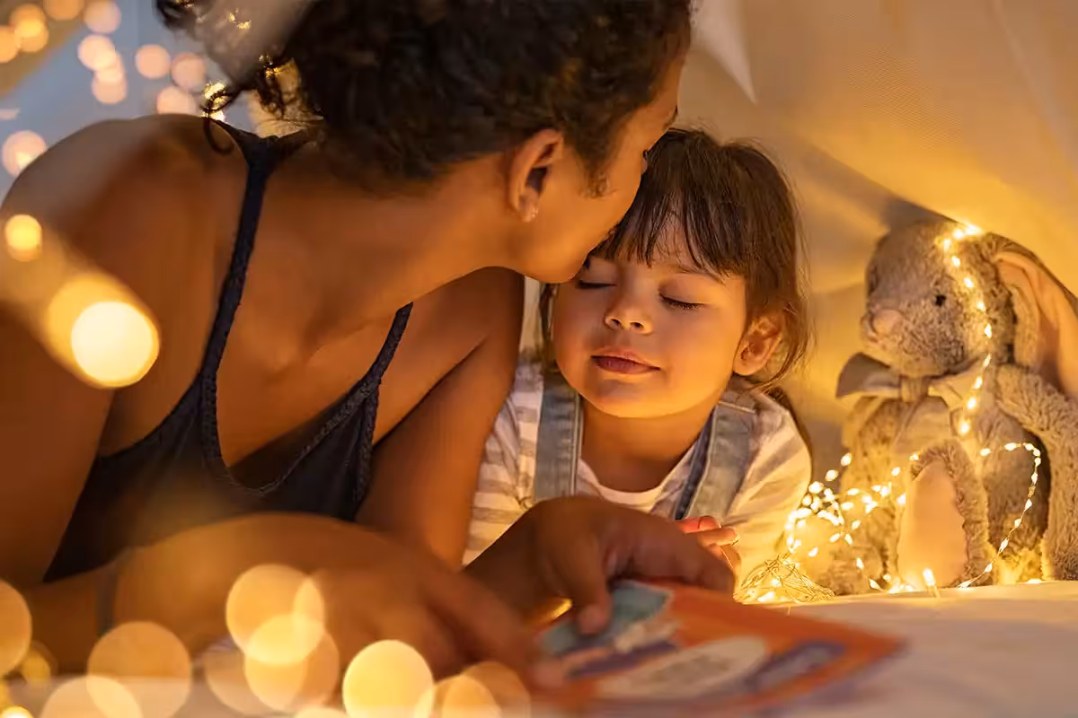 Loving mother kissing daughter in cozy blanket tent.