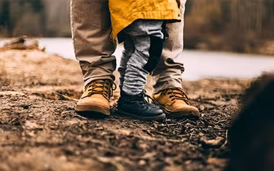 Legs and feet of father and small son standing in woods wearing walking shoes. Benefits of life insurance.