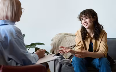 Young smiling woman talking to therapist while she making notes in document. Psychiatrist vs Psychologist.