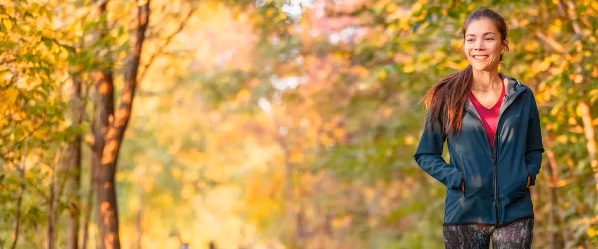 Happy young woman wearing exercise clothing walking on a path through trees in autumn. Bupa's Mental Health Insurance & Support In The UK