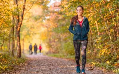 Happy young woman wearing exercise clothing walking on a path through trees in autumn. Bupa's Mental Health Insurance & Support In The UK