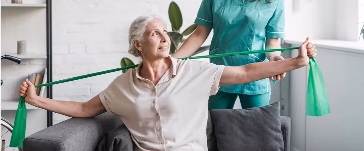 Senior woman with stretch band being assist by female physiotherapist. Health Insurance With Complementary Alternative Therapy Cover