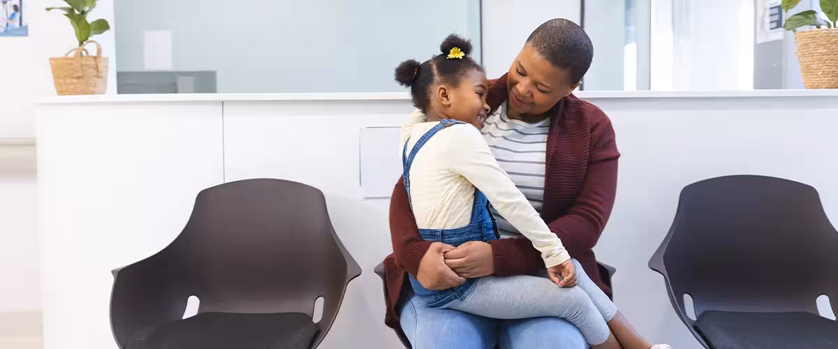 Happy african american mother and daughter sitting in waiting room at hospital. Comprehensive vs Basic Health Insurance - What's The Difference?