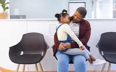 Happy african american mother and daughter sitting in waiting room at hospital. Comprehensive vs Basic Health Insurance - What's The Difference?