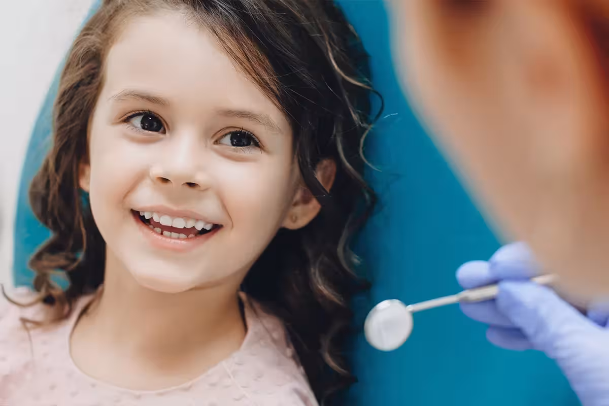 Curly haired little girl looking and smiling to the dentist after a checking up