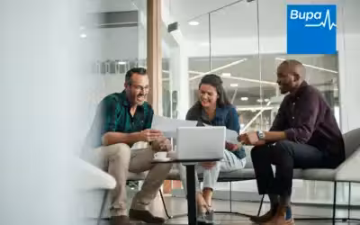 Group of business people sat around a table working from a laptop. Bupa Corporate Health Insurance - Group Cover Explained