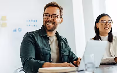 Man and a woman sat at a desk with laptop. What Is Income Protection Insurance