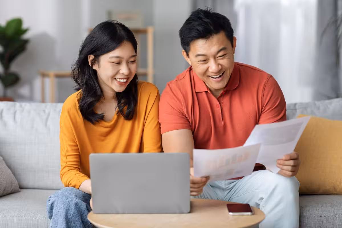 happy asian spouses paying bills online using laptop