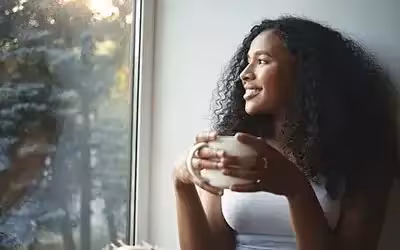 happy woman looking out of her window thinking about the benefits of income protection insurance