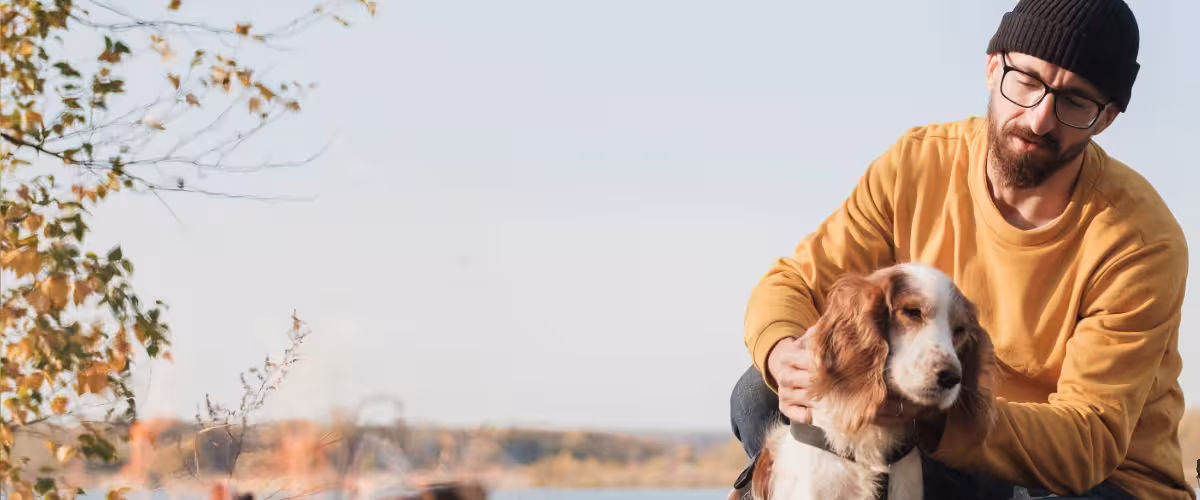 Man hugs his dog sitting by the lake, thinking about how cancer can affect life insurance.