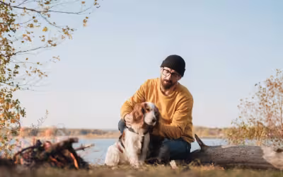 Man hugs his dog sitting by the lake, thinking about how cancer can affect life insurance.