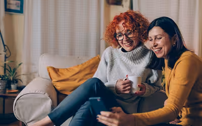 Middle aged female friends at home, using mobile phone to learn more about life insurance