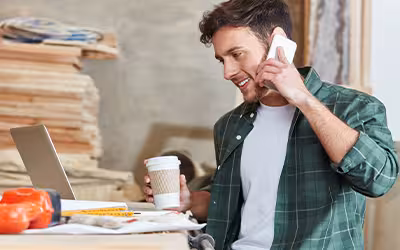 Tradesperson on his phone and laptop smiling whilst sorting his income protection insurance 