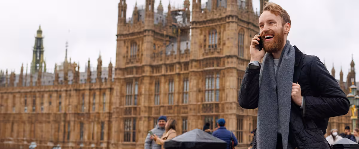 Laughing man talking on the phone while standing against the background of the Big Ben tower on Westminster Bridge