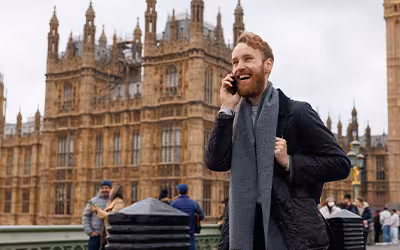 Laughing man talking on the phone while standing against the background of the Big Ben tower on Westminster Bridge