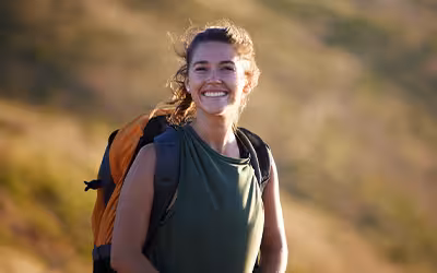 Smiling woman with a backpack hiking on a sunlit grassy hillside