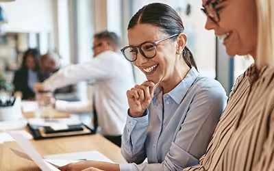 Two colleagues in an office reviewing documents together and smiling, representing employees considering their health insurance options after leaving a job