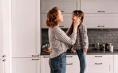 Mother and young daughter laugh while baking together in a bright kitchen