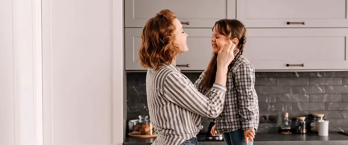 Mother and young daughter laugh while baking together in a bright kitchen