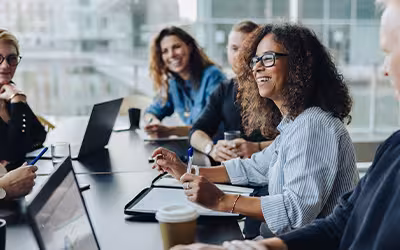 Colleagues smiling around a boardroom table with laptops during a company meeting