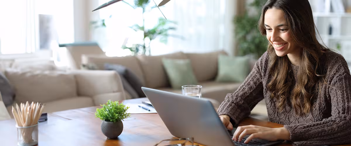 A young woman smiling while completing a life insurance application on her laptop at home