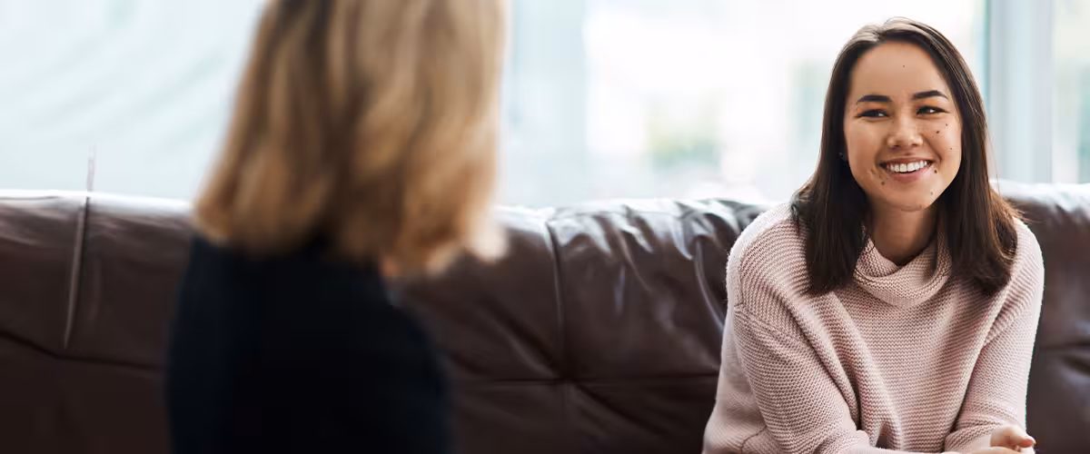 Smiling woman talks with another person on a sofa, with the Vitality logo overlaid