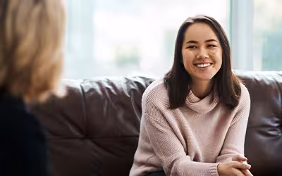 Smiling woman talks with another person on a sofa, with the Vitality logo overlaid