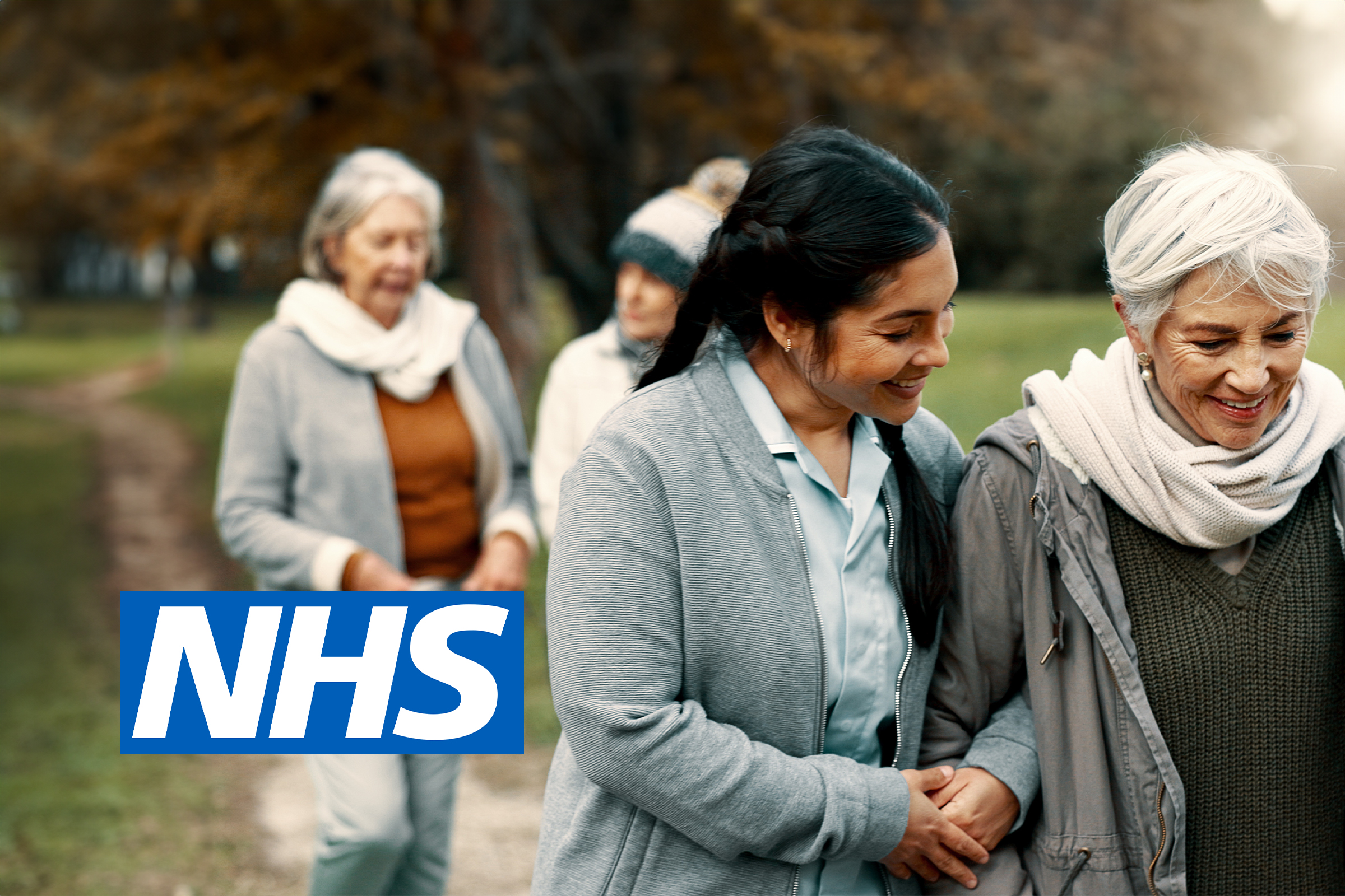Carer walking arm in arm with older women in a park, with the NHS logo overlaid