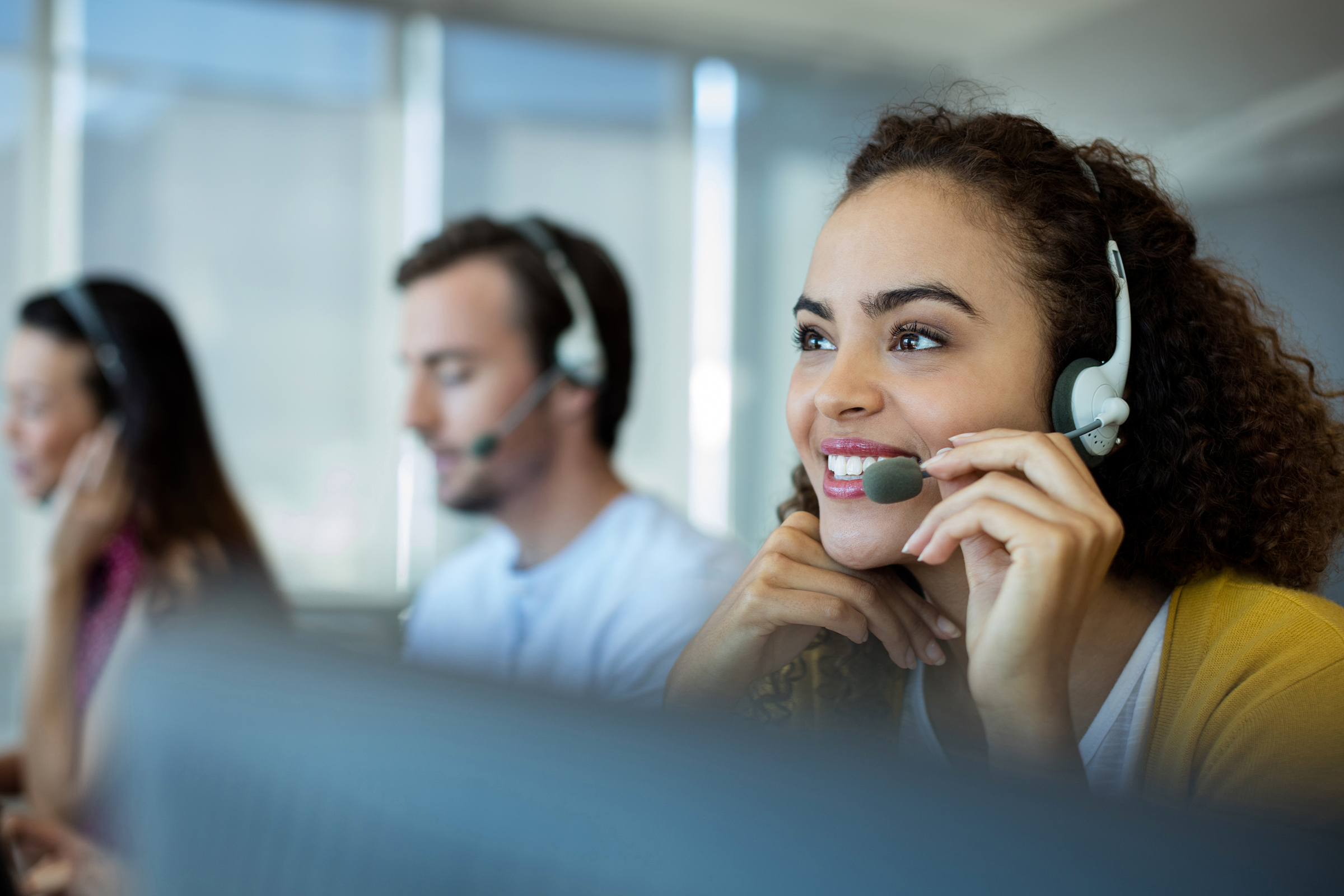 Smiling customer service agent wearing a headset in a busy call centre