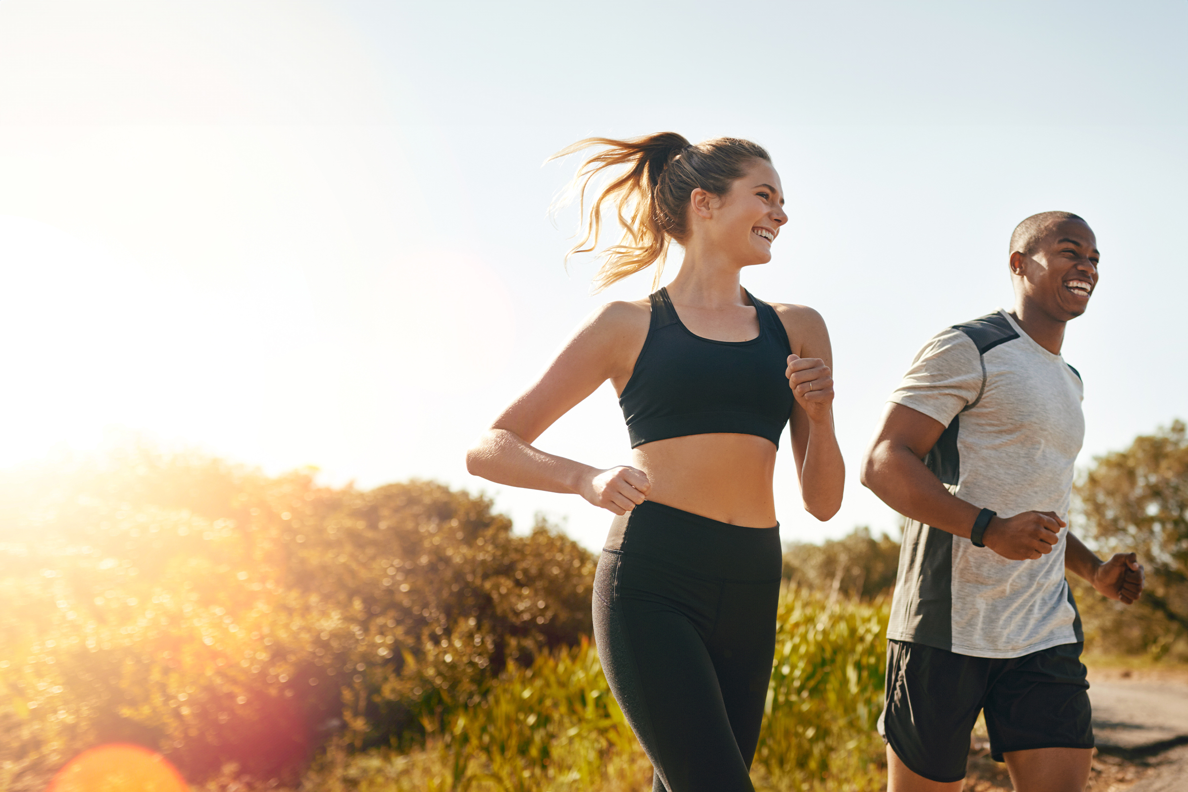 Smiling woman and man jog along a country path in bright sunshine