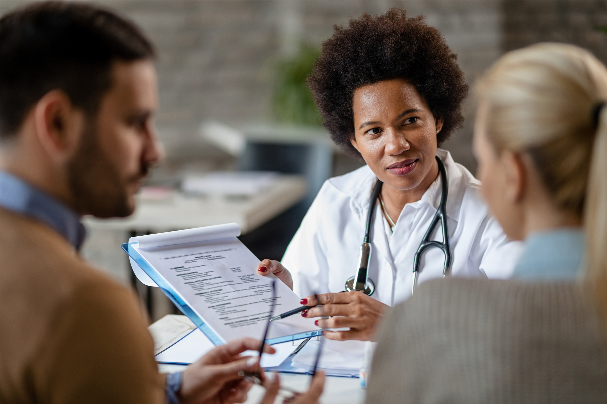 Doctor with a stethoscope discussing a policy document with a couple in a consultation