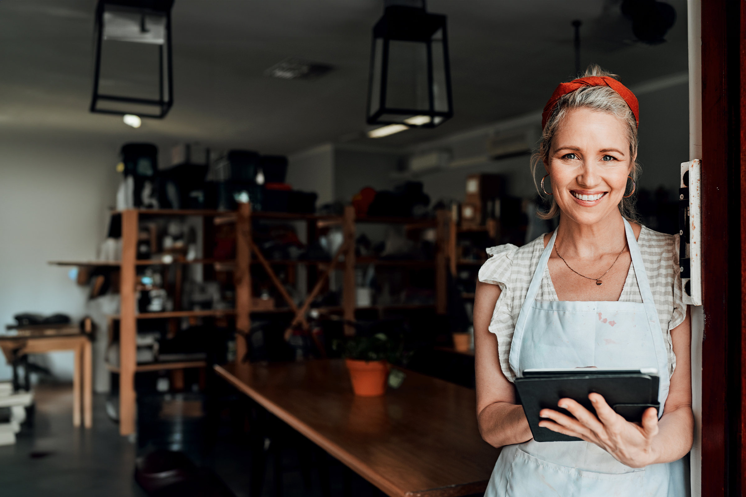 Smiling small business owner in an apron holds a tablet in her workshop doorway