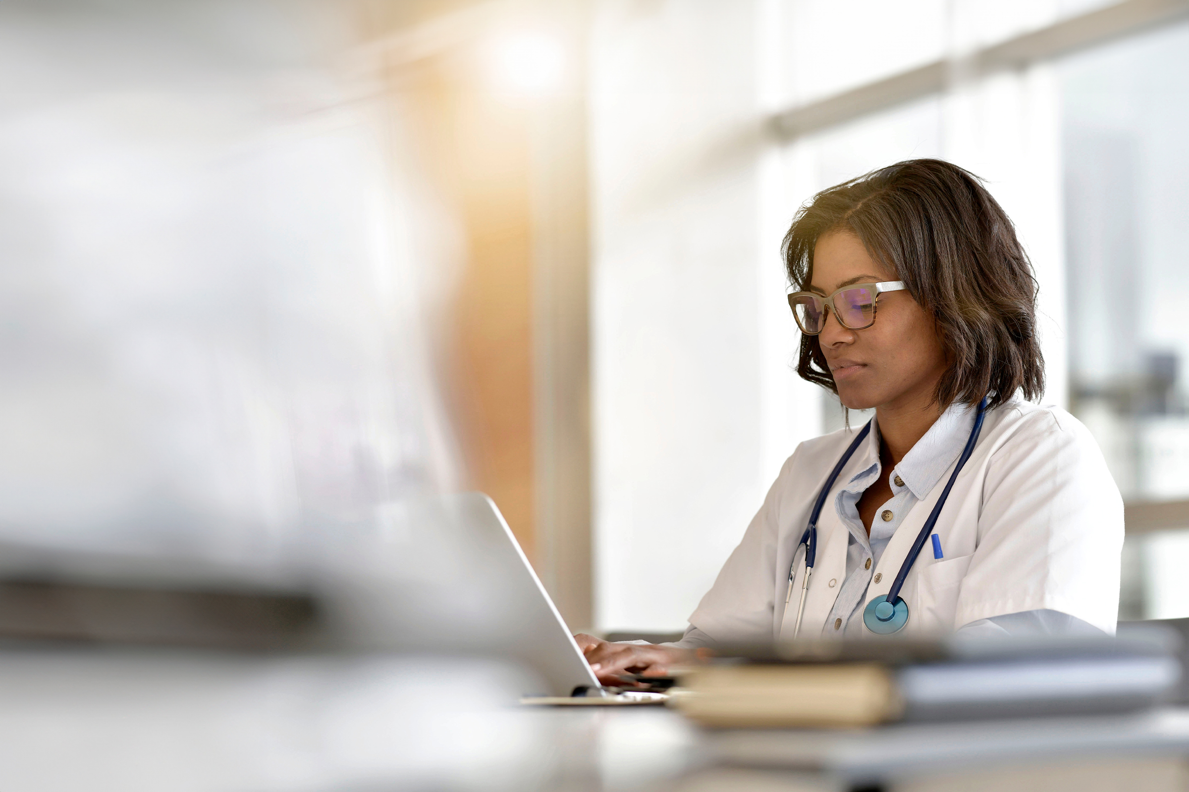Female doctor in a white coat with a stethoscope working on a laptop at her desk