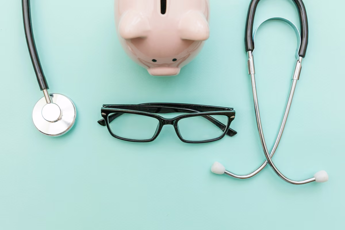 Stethoscope, piggy bank and glasses arranged on a mint green background