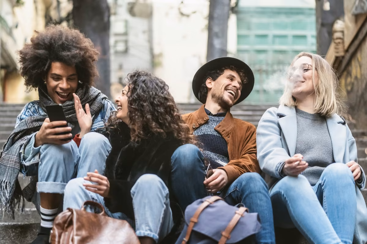 Young friends using phones, smoking and talking together outdoor