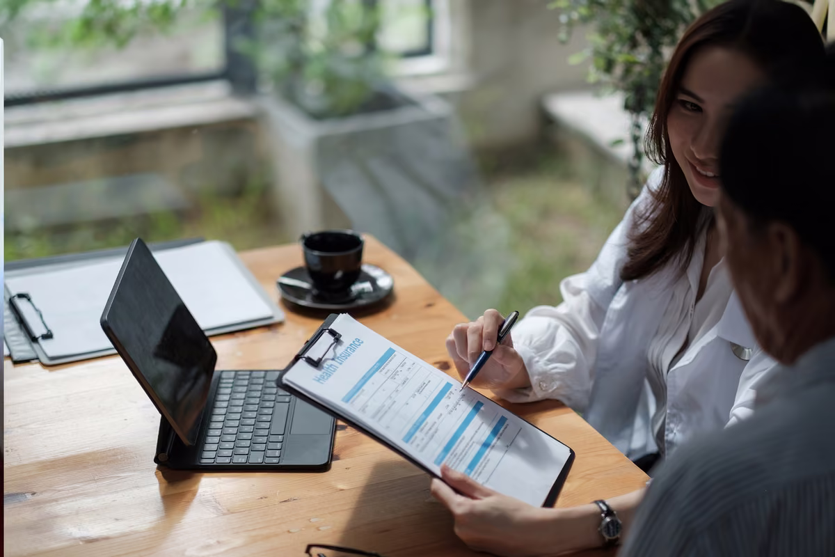 Adviser pointing a pen at a health insurance document while a man reviews it at a desk