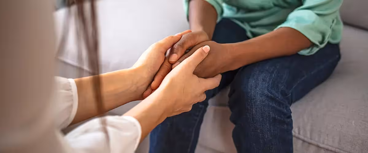 Two people holding hands on a sofa during a supportive conversation