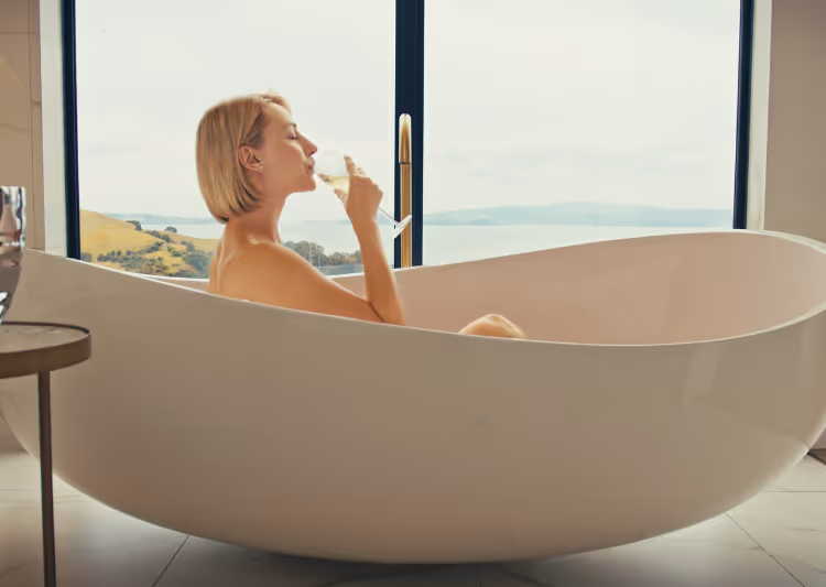 A guest at Omana having sparkling wine in the bathtub with an ocean view