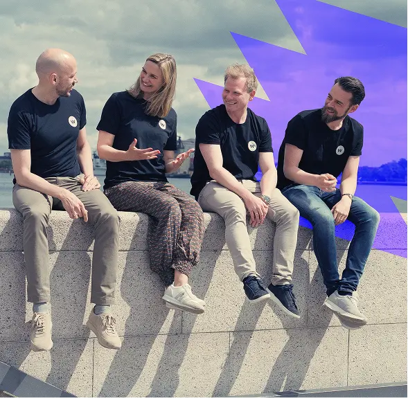 Four people wearing black shirts sitting on a stone ledge, talking and smiling outdoors.