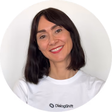 Smiling woman with dark hair wearing a white DialogShift shirt on white background.
